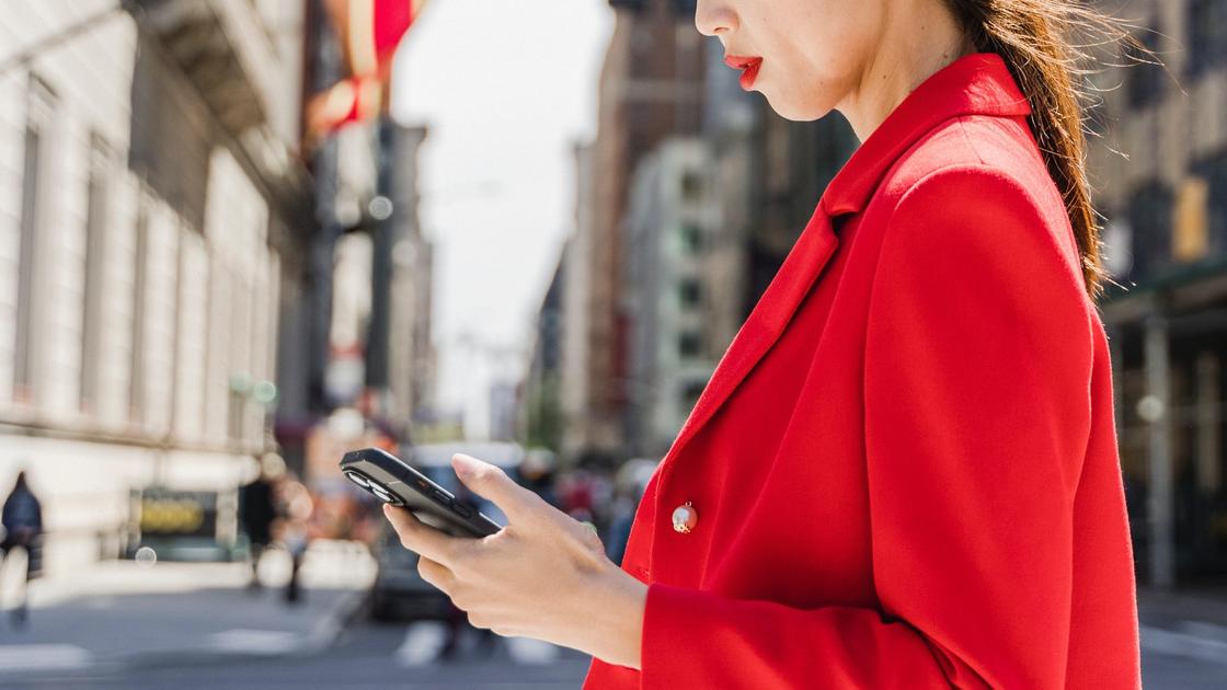 Девушка в красном переходит дорогу с телефоном в руках